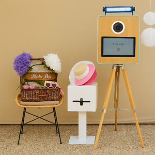 Fotobooth met accessoires in een feestelijke setting, inclusief hoeden, bloemen en een touchscreen camera op statief